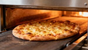 Pizza emerging from a conveyor oven, golden and crisp.