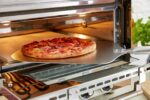 Pizza going into a King Edward Pizza King oven on its cordierite stone